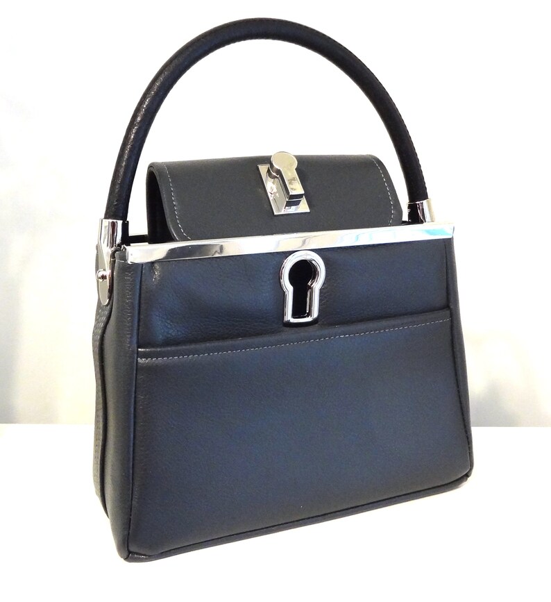 May include: A dark gray leather handbag with a silver top clasp and a silver keyhole detail. The bag has a black leather top handle.