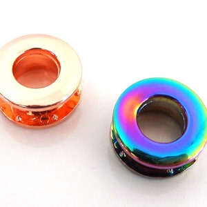 Può includere: Due occhielli metallici, uno in oro rosa e uno con una finitura arcobaleno iridescente. Entrambi gli occhielli sono rotondi con un foro al centro.