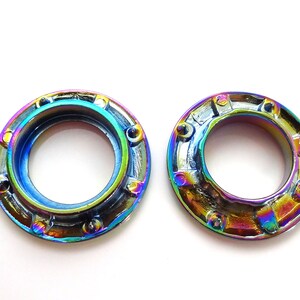 K&ouml;nnte beinhalten: Zwei regenbogenfarbene Metallstifte mit einem runden Loch in der Mitte. Die Stifte haben einen strukturierten, leicht erh&ouml;hten Au&szlig;enrand.