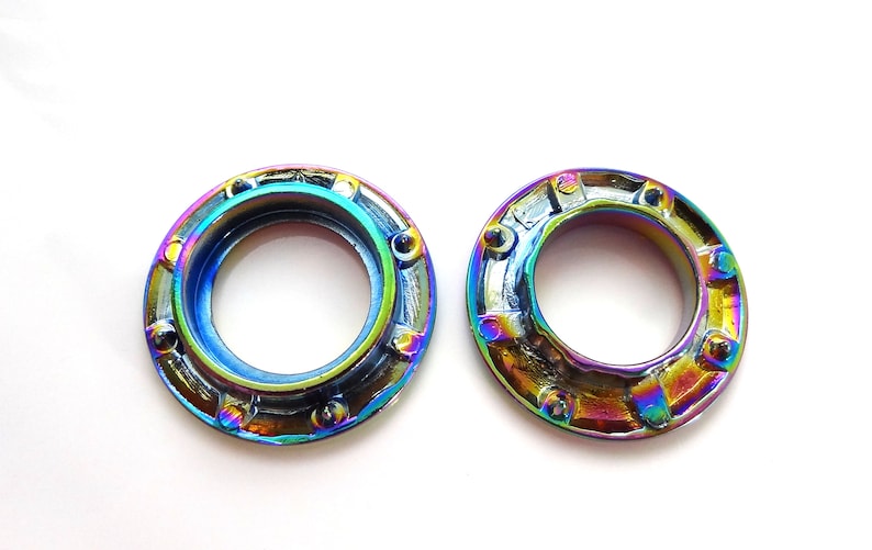 K&ouml;nnte beinhalten: Zwei regenbogenfarbene Metallstifte mit einem runden Loch in der Mitte. Die Stifte haben einen strukturierten, leicht erh&ouml;hten Au&szlig;enrand.