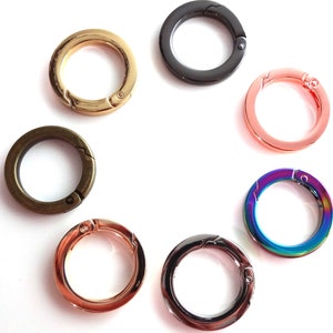 Könnte beinhalten: Sortiment von sieben Schlüsselringen aus Metall in verschiedenen Farben, darunter Gold, Silber, Schwarz, Roségold und Regenbogen.