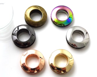 Könnte beinhalten: Sechs Metallösen in verschiedenen Farben und Ausführungen, darunter Gold, Silber, Schwarz und schillernd. Die Ösen sind rund mit einem Loch in der Mitte.