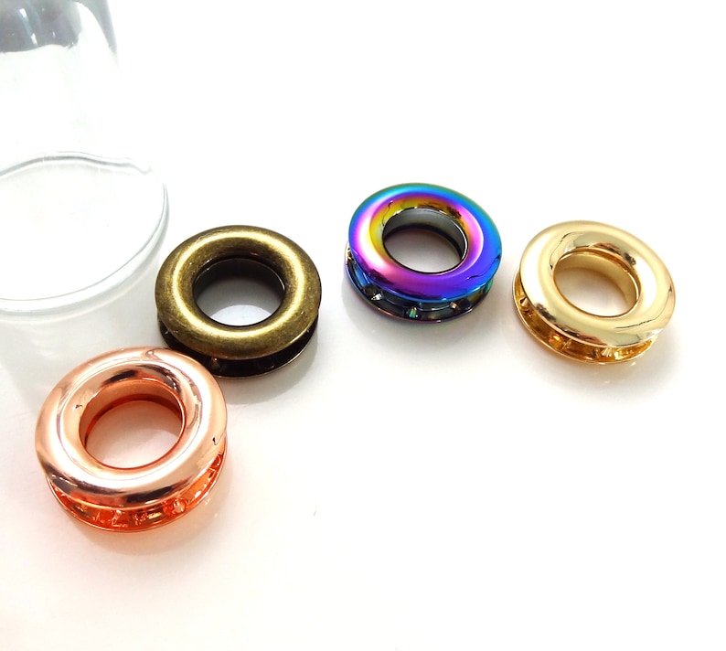 K&ouml;nnte beinhalten: Vier Metall&ouml;sen in verschiedenen Farben: Gold, Bronze, regenbogenfarben und Kupfer. Die &Ouml;sen sind rund mit einem Loch in der Mitte.