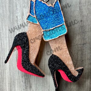 May include: A pair of black high-heeled shoes with red soles and a pair of blue denim jeans with glitter. The shoes and jeans are attached to a red and white polka dot ornament.