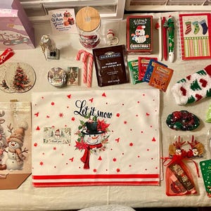 May include: A collection of Christmas-themed items, including a snowman-themed tea towel, a red and white sock, a Santa Claus card, and a "Let it snow" sleep mask. Other items include candy canes, hot cocoa mix, and decorative ornaments.