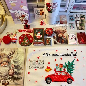 May include: A collection of Christmas-themed items, including a mug with "Merry Christmas" text, ornaments, gift tags, a red car with a Christmas tree, and a Santa Claus figure. The items are arranged on a white surface.