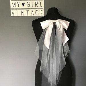 May include: White bridal veil with a large satin bow on a black dress form. The sign behind the veil reads "ME & MY ♥ GIRL VINTAGE".