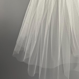 May include: A white tulle bridal veil with a single layer of fabric. The veil is pleated and has a scalloped edge.
