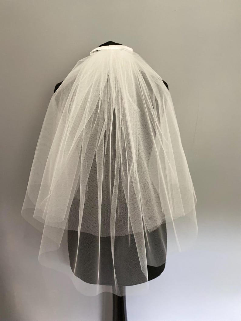 May include: A white single-tier bridal veil with a satin ribbon trim. The veil is made of soft tulle and is designed to be worn with a comb.