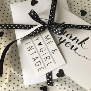 May include: A white gift bag with a black and white polka dot pattern. The bag is tied with a black ribbon with white polka dots and a small black heart charm. The bag is decorated with a white card that says "Me & My Girl Vintage" and a white card that says "Thank you".