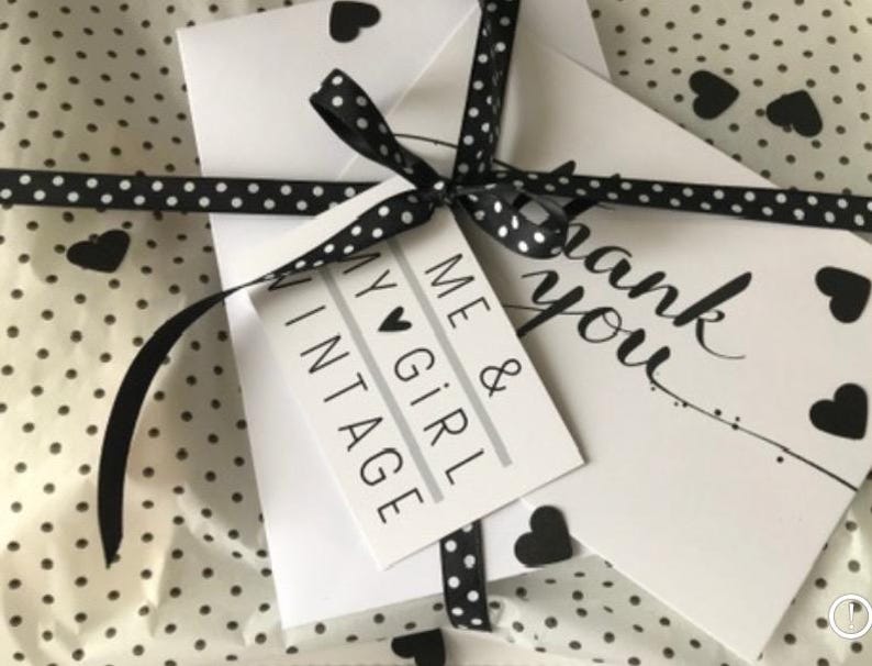 May include: A white gift bag with a black and white polka dot pattern. The bag is tied with a black ribbon with white polka dots and a small black heart charm. The bag is decorated with a white card that says "Me & My Girl Vintage" and a white card that says "Thank you".