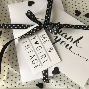 May include: A gift wrapped in white polka dot tissue paper, tied with a black and white polka dot ribbon. The gift includes a tag that says "ME & GIRL VINTAGE" and a card that says "thank you". Black heart-shaped stickers are scattered around.