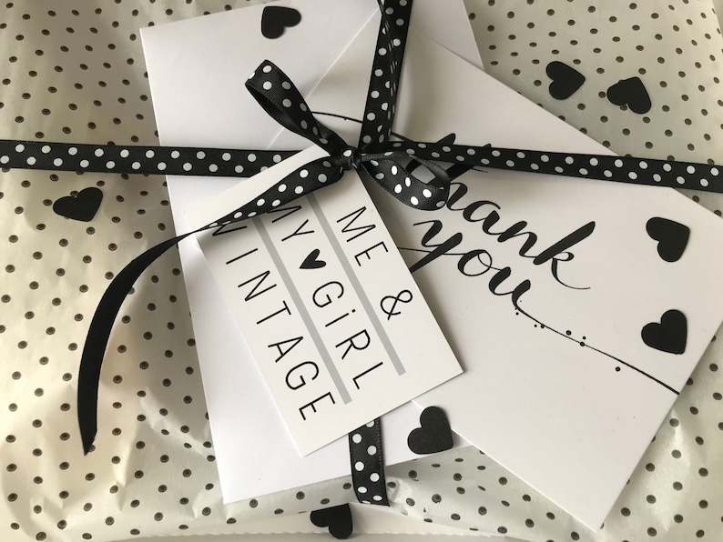 May include: A gift wrapped in white polka dot tissue paper, tied with a black and white polka dot ribbon. The gift includes a tag that says "ME & GIRL VINTAGE" and a card that says "thank you". Black heart-shaped stickers are scattered around.