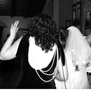 May include: Black velvet dress with a white back panel and a pearl necklace design. A bride in a white wedding dress and veil is visible. The image is in black and white.