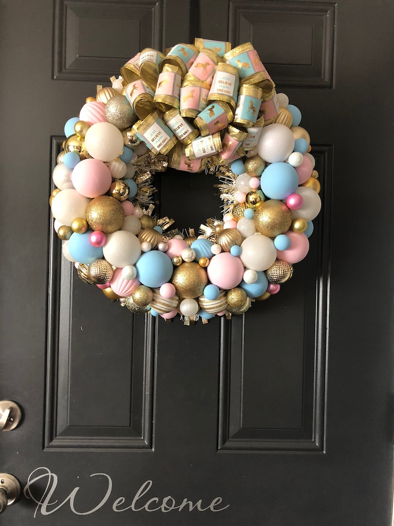 May include: A pink and blue Christmas wreath with gold ornaments and a bow with the text "Believe in Magic" and "Believe in Dreams".