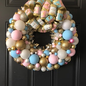 May include: A pink and blue Christmas wreath decorated with gold ornaments and a large bow with the text "Just Believe in Your Dreams".