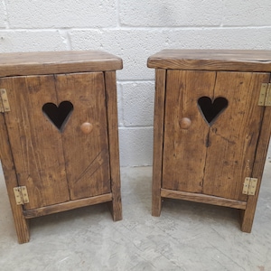 May include: Two rustic wooden bedside tables with heart-shaped cutouts and brass hinges. Each bedside table has a single door and a knob.