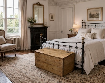 May include: A bedroom with a wrought iron bed, a wooden chest, and a patterned rug. The room has a fireplace, a mirror, and a window with curtains. The walls are painted white, and the room has a classic, vintage feel.