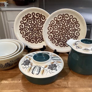 Könnte beinhalten: Ein Set Vintage-Küchenutensilien mit einem braunen und weißen Blumenmuster. Das Set enthält zwei große Teller, eine kleine Auflaufform mit Deckel und drei ineinander verschachtelte Schüsseln.