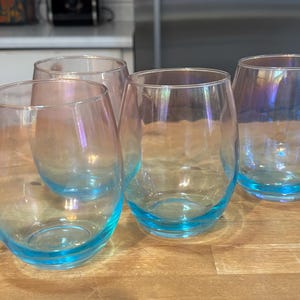 Puede incluir: Cuatro vasos de vidrio iridiscente con un borde azul claro. Los vasos están vacíos y están sobre una superficie de madera.
