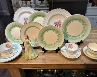 Puede incluir: Un juego de platos y tazas de té de porcelana vintage de color verde y blanco con diseños florales. El juego incluye una taza de té y un platillo, un plato pequeño y varios platos grandes.