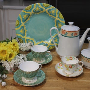 Könnte beinhalten: Eine Servierplatte mit türkisfarbenem und gelbem Muster mit einer weißen Teekanne, einer Milchkännchen, einer Zuckerdose und drei Teetassen und Untertassen. Die Teetassen und Untertassen haben ein grünes und goldenes Muster, während die Teekanne, die Milchkännchen und die Zuckerdose ein Blumenmuster mit roten, orangefarbenen und grünen Akzenten haben.