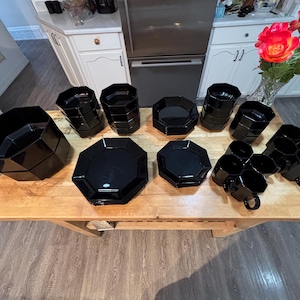 Peut inclure: Un ensemble de vaisselle en verre noir aux formes octogonales, comprenant un grand saladier, plusieurs bols plus petits, des assiettes plates et un ensemble de tasses avec anses. Les pièces sont disposées en groupes sur une surface en bois.
