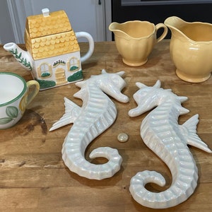 Peut inclure: Un ensemble de quatre tasses à thé et une théière en céramique, avec un motif de cottage jaune et blanc. Deux figurines de cheval de mer en céramique blanche sont également incluses.