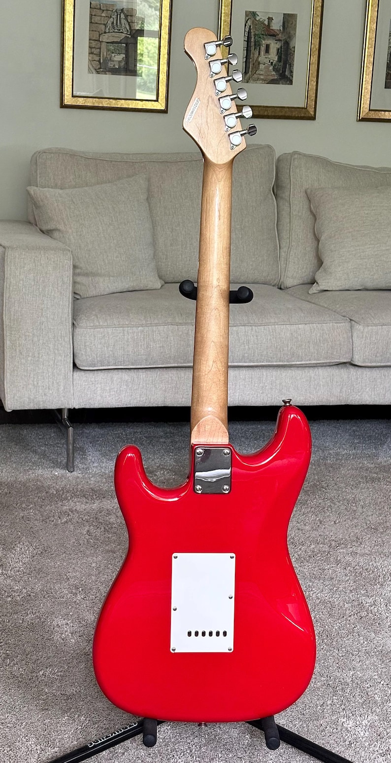 May include: A bright red electric guitar shown from the back, featuring a smooth glossy finish, a light-colored wooden neck, a chrome neck plate, and a white rectangular back plate with six string holes. The headstock includes silver tuning pegs.