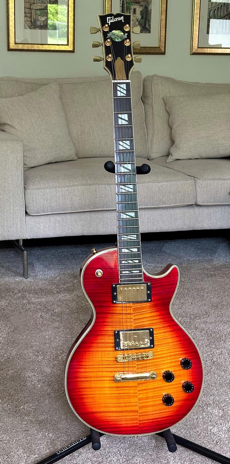 May include: A Gibson electric guitar with a cherry sunburst finish on a flamed maple top. The instrument features gold hardware, two humbucker pickups, a tune-o-matic bridge, four black control knobs, and a dark fretboard with trapezoid inlays.
