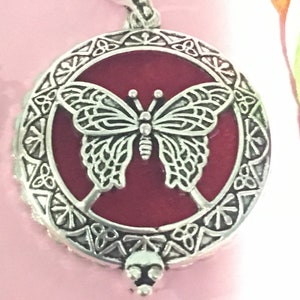 May include: A silver pendant with a red enamel butterfly design. The pendant has a detailed ornate border and a skull-shaped bail.