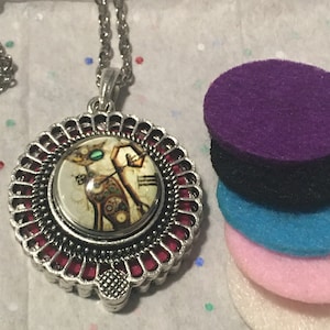 Puede incluir: Un collar de plata con un colgante redondo que presenta un diseño de gato estilo steampunk. El colgante tiene un borde rojo y una cubierta de vidrio transparente. El collar viene con cuatro almohadillas de fieltro en morado, negro, azul y rosa.