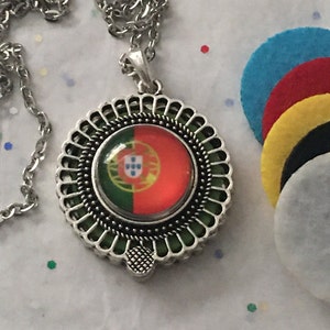 Può includere: Una collana d'argento con un ciondolo rotondo che presenta la bandiera del Portogallo. Il ciondolo ha un bordo decorativo e uno sfondo verde.