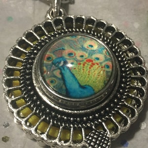 Peut inclure: Un collier avec un pendentif en argent avec un motif de filigrane jaune et noir. Le pendentif présente un cabochon rond en verre avec une image de paon colorée.