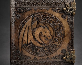 May include: A rectangular brown leather journal featuring an embossed dragon design centered within a circular frame. The cover is decorated with intricate border patterns and secured by two antique brass-colored metal latches on the right side.