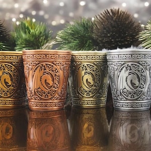 Könnte beinhalten: Vier Metall-Schnapsgläser mit einem geprägten Drachen-Design. Die Gläser sind in Gold, Kupfer, Silber und Zinn.