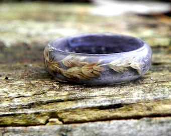 May include: A purple resin ring with dried flowers and grasses embedded inside. The ring is sitting on a piece of weathered wood.