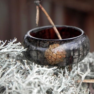 May include: A black and brown wooden ring with a natural wood design. The ring has a unique texture and a natural wood grain pattern.