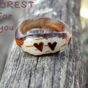 May include: A clear resin ring with a wood-like texture and two brown hearts. The text "FOREST for you" is visible in the background.