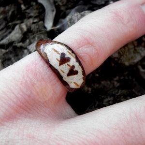 May include: A brown ring with a white band and two hearts carved into it. The ring is worn on a finger.