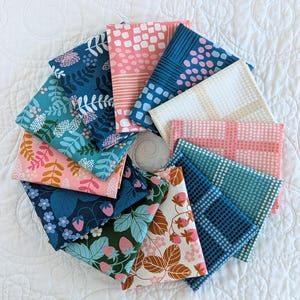 May include: A selection of folded fabric squares featuring floral and geometric designs. The colour scheme includes pink, blue, green, and white. The fabrics are arranged in a circular pattern on a white quilted surface.