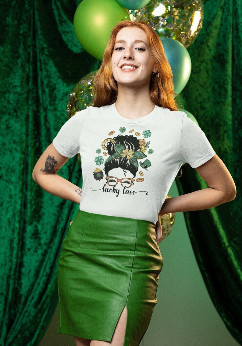 May include: White t-shirt with a St. Patrick's Day design featuring a woman's hairstyle with shamrocks, a pot of gold, and the text "lucky lass." The woman is wearing a green leather skirt.