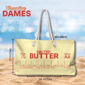 May include: A yellow canvas tote bag with rope handles. The bag has a red and white label that says "Salted Butter" and "Grade AA". The label also has a measurement guide for tablespoons and cups. The bag is 13 inches tall and 24 inches wide.