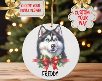 May include: A white ceramic Christmas ornament featuring a detailed portrait of a Husky dog with blue eyes, black and white fur, and a red bow. The name "FREDDY" is printed below the dog. The ornament has a gold string for hanging.