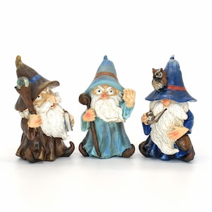 Può includere: Tre figurine di gnomi blu e marroni con barbe bianche. Gli gnomi indossano cappelli blu e hanno accessori diversi, tra cui un bastone, una pipa e un gufo.