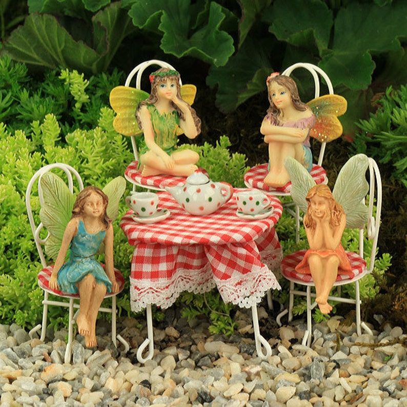 May include: Four fairies are sitting at a miniature red and white checkered table with a white lace trim. The table has a teapot and teacups with polka dots. The fairies are wearing colorful dresses and have wings.