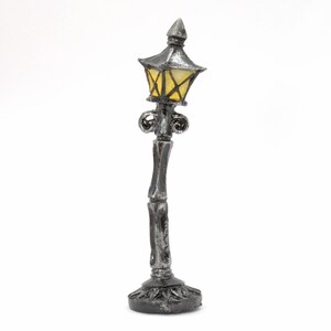 May include: A miniature silver lamp post with a yellow glass lampshade. The lamp post has a decorative base and ornate details.