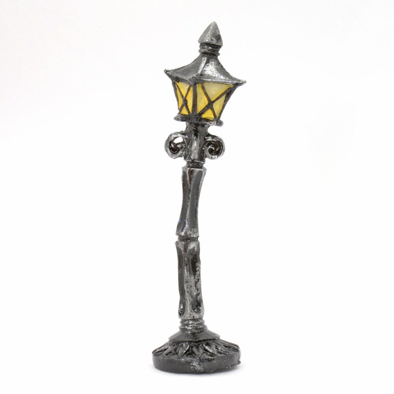 May include: A miniature silver lamp post with a yellow glass lampshade. The lamp post has a decorative base and ornate details.