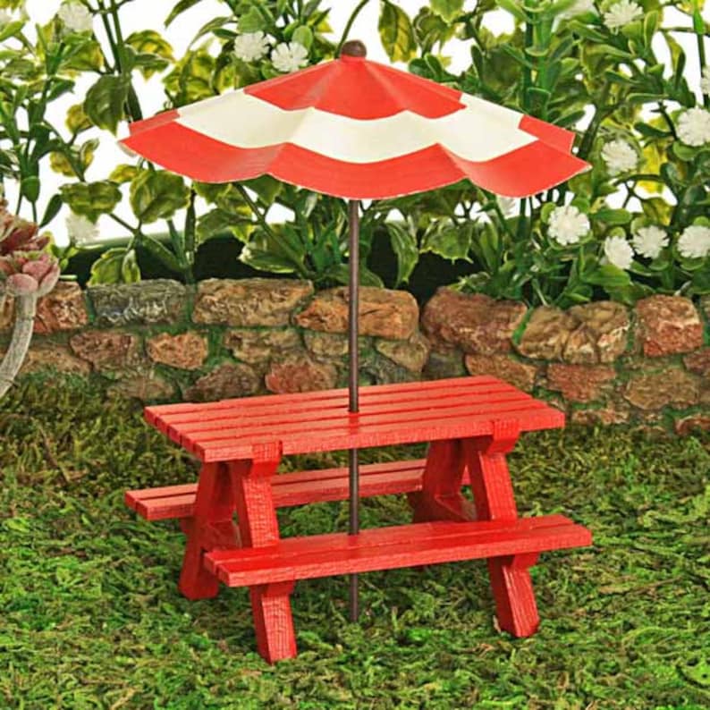 Puede incluir: Una mesa de picnic roja en miniatura con una sombrilla a rayas rojas y blancas. La mesa y la sombrilla est&aacute;n instaladas en un lecho de musgo verde.