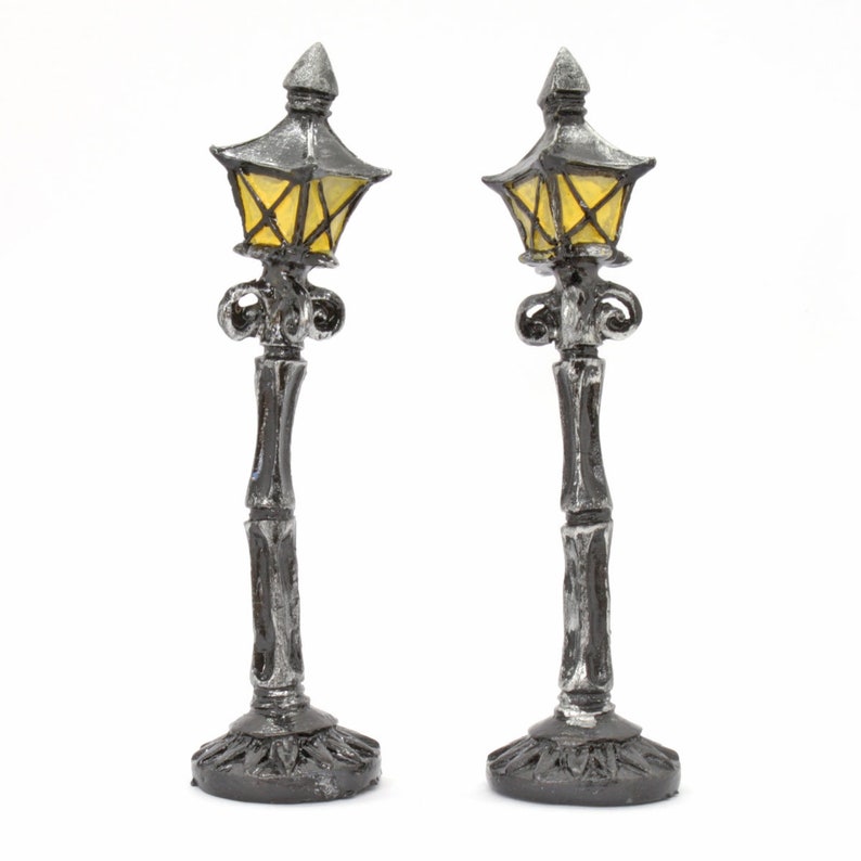 May include: Two black metal lamp posts with yellow glass lampshades. The lamp posts are decorative and have a vintage style.